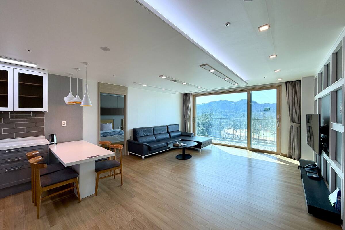 Een moderne woonkamer met een bank, een eethoek met een tafel en stoelen, en een keuken met kasten en een koffieapparaat.