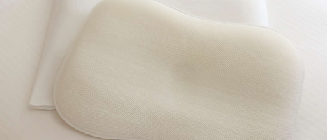 Un almohadón blanco y una sábana blanca doblada sobre una cama.