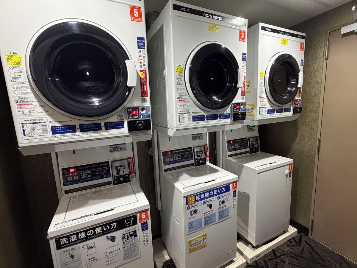 A row of stacked laundry machines in a hotel room.