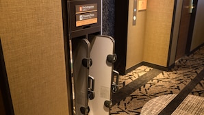 Pasillo de hotel con extintor y señal de plancha para pantalones en la pared.