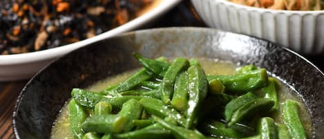 Un tazón de verduras verdes en caldo, con otros platos al fondo.