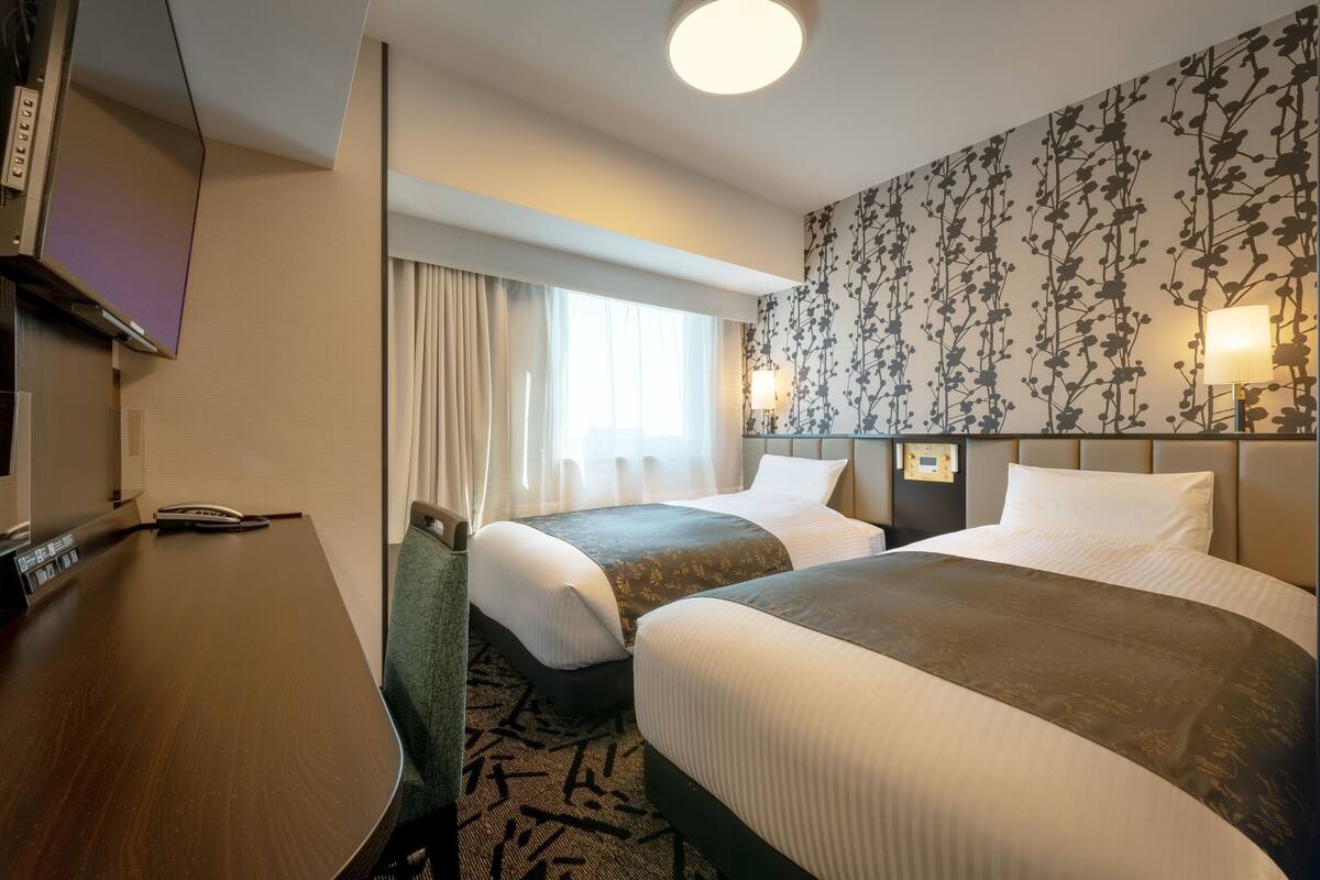 Une chambre d’hôtel avec deux lits, un bureau, une télévision et une fenêtre avec des rideaux.