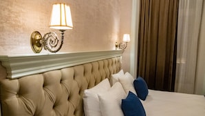 A bed with a tufted headboard, two wall sconces, and a window with curtains. - La Casa Sahil Hotel (Baku)