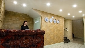A reception area with a patterned counter, a brick wall, and a staircase leading to an upper floor. - La Casa Sahil Hotel (Baku)