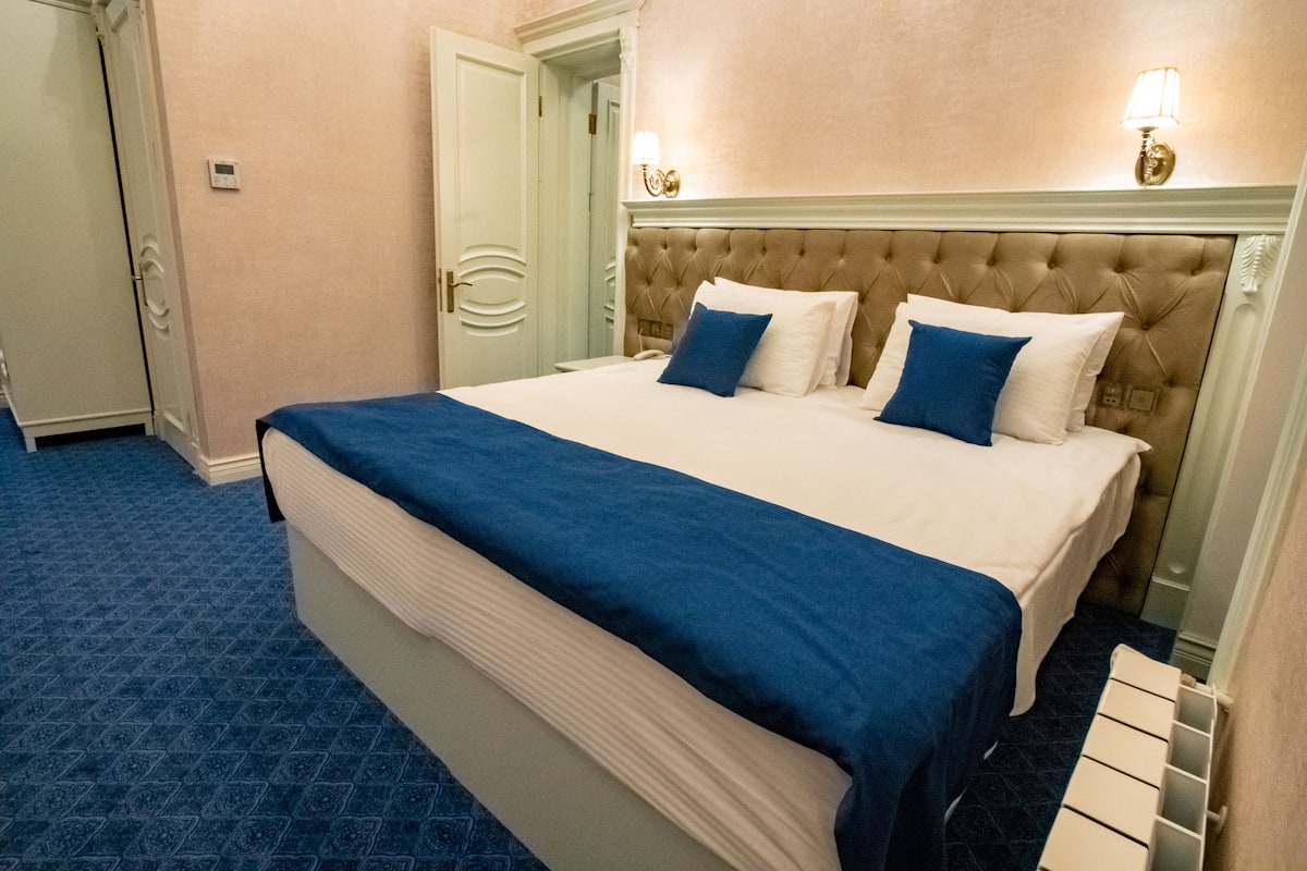 Ein Hotelzimmer mit einem großen Bett, einem blauen Teppich, einem weißen Kopfteil und zwei Wandlampen.