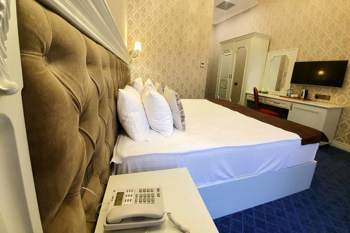 Ein Hotelzimmer mit einem großen Bett, einem Nachttischtelefon, einem Kleiderschrank, einem Spiegel und einem Fernseher.