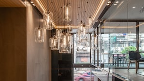 A modern interior with a long reception desk, seating area, and large windows offering a view of the street. - The Quarter Phromphong by UHG (Bangkok)