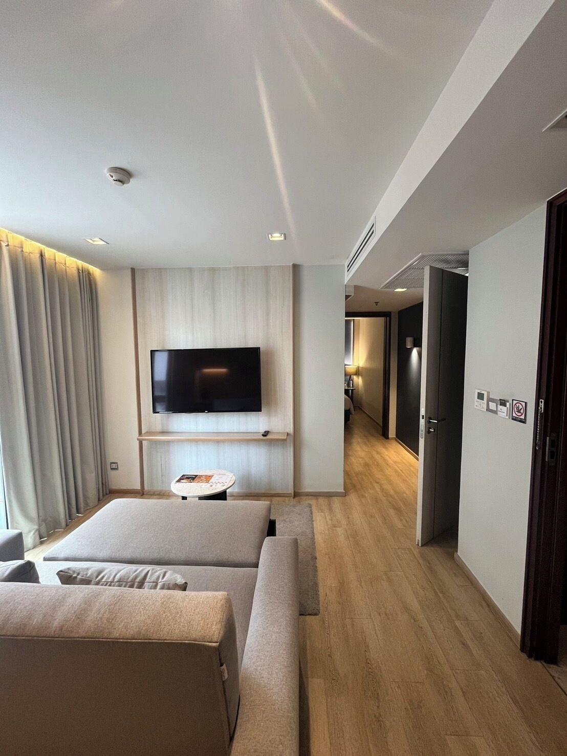 A modern hotel room with a large flat-screen TV mounted on the wall, a sofa, a small round table, and a wooden floor.
