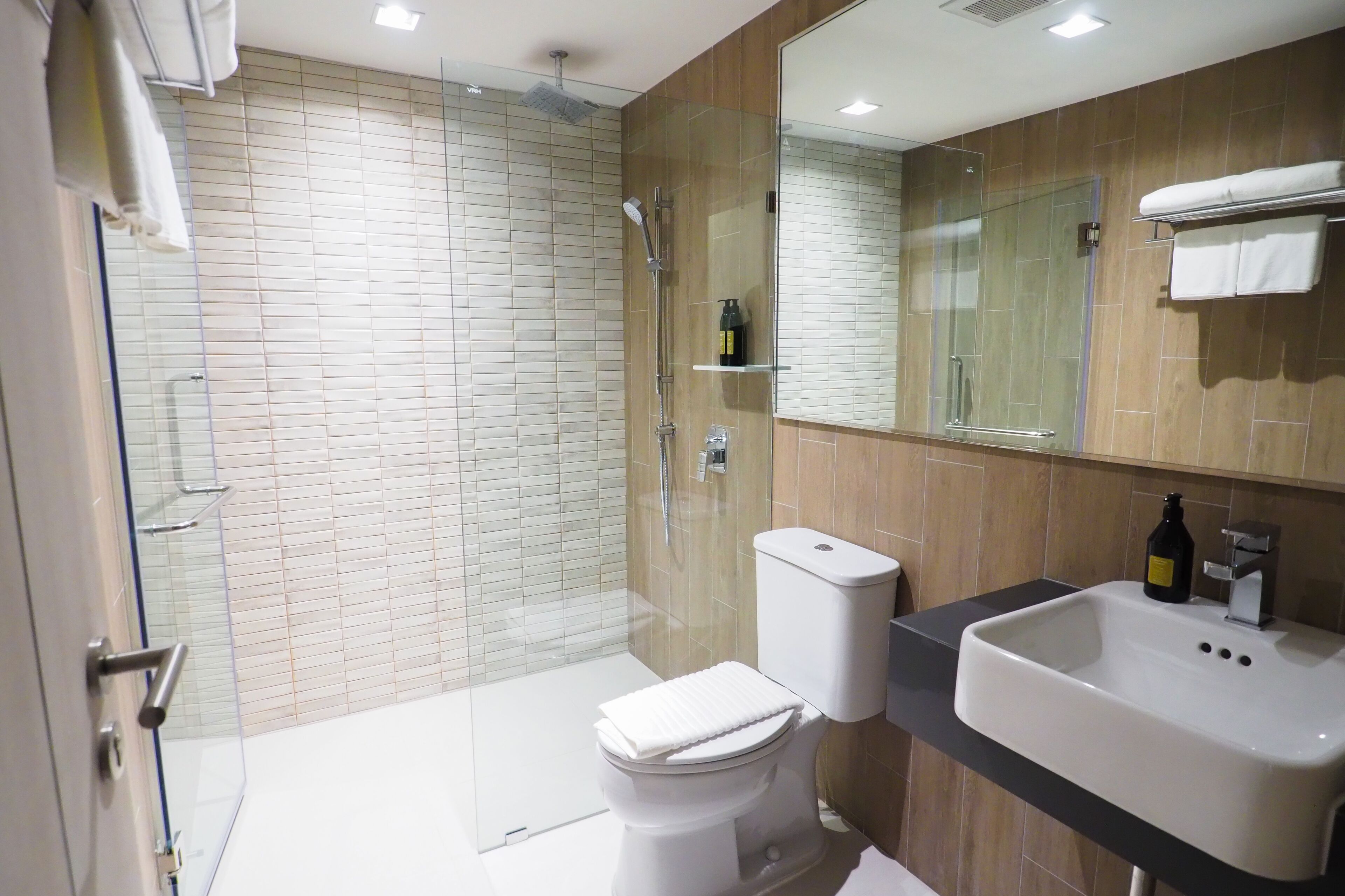 Un baño moderno con ducha de vidrio, inodoro blanco y lavabo con espejo superior.
