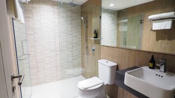 Un baño moderno con ducha de vidrio, inodoro blanco y lavabo con espejo superior.