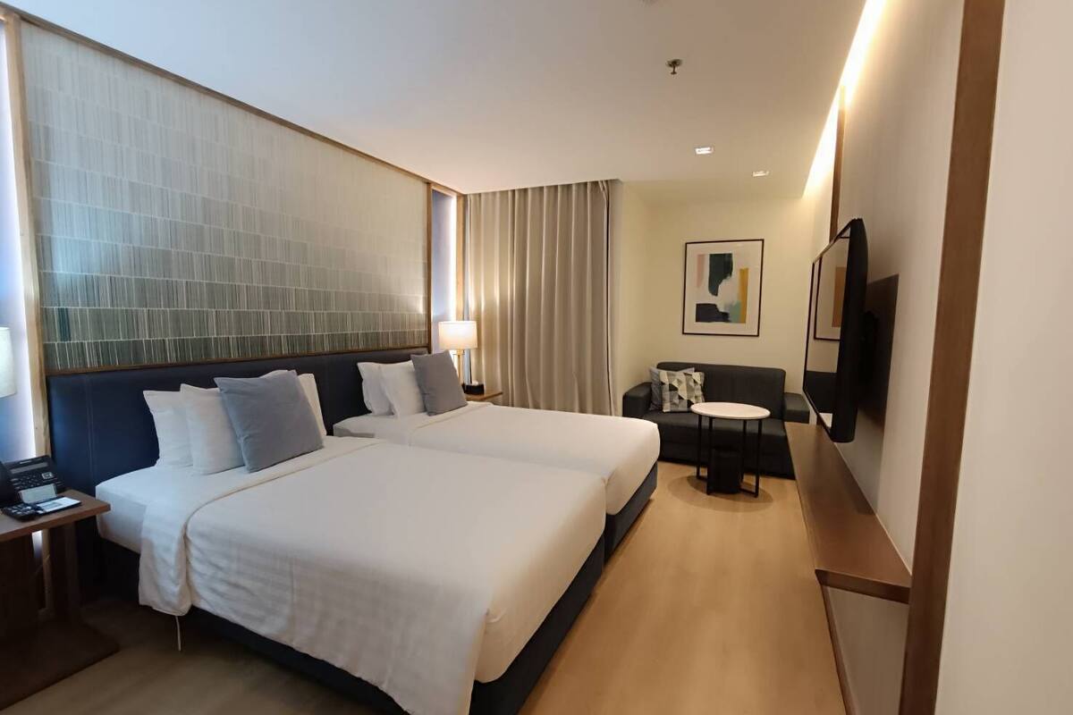 A hotel room with a large bed, a desk, a chair, a TV, and a large window with curtains.