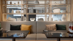 A modern interior with a sofa and a dining table, a glass display case with various items, and a kitchen area in the background. - The Quarter Phromphong by UHG (Bangkok)