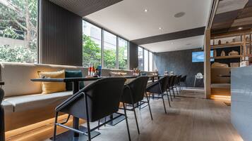 A modern restaurant with a long counter, black chairs, and a sofa with cushions.