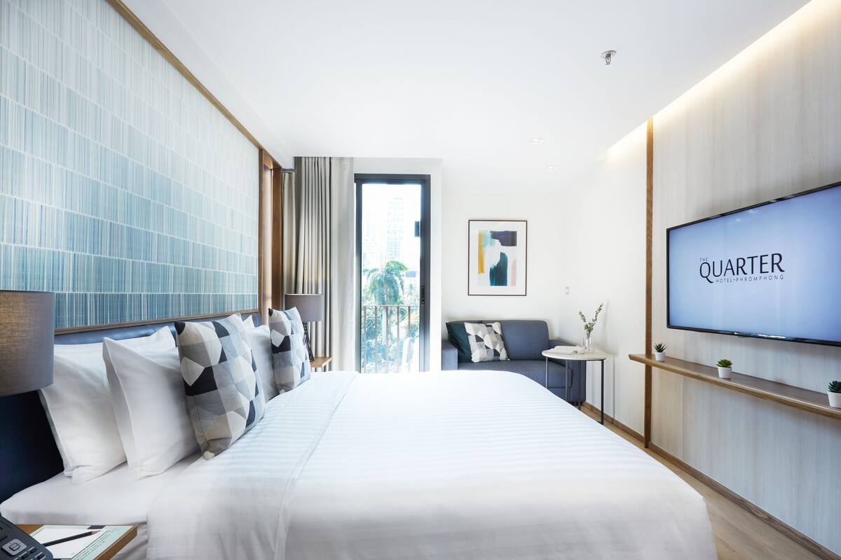 A modern hotel room with a large bed, a TV, a desk, and a view of the outdoors.