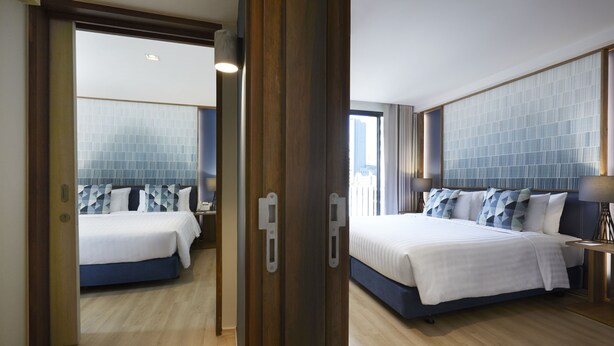A hotel room with two beds, a large window, and a view of the city. - The Quarter Phromphong by UHG (Bangkok)
