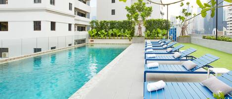 A swimming pool with blue lounge chairs and a white building in the background.
