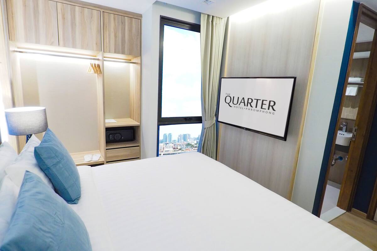 A hotel room with a large bed, a wardrobe, a mirror, and a sign that reads "QUARTER HOTEL PHROMPHONG".