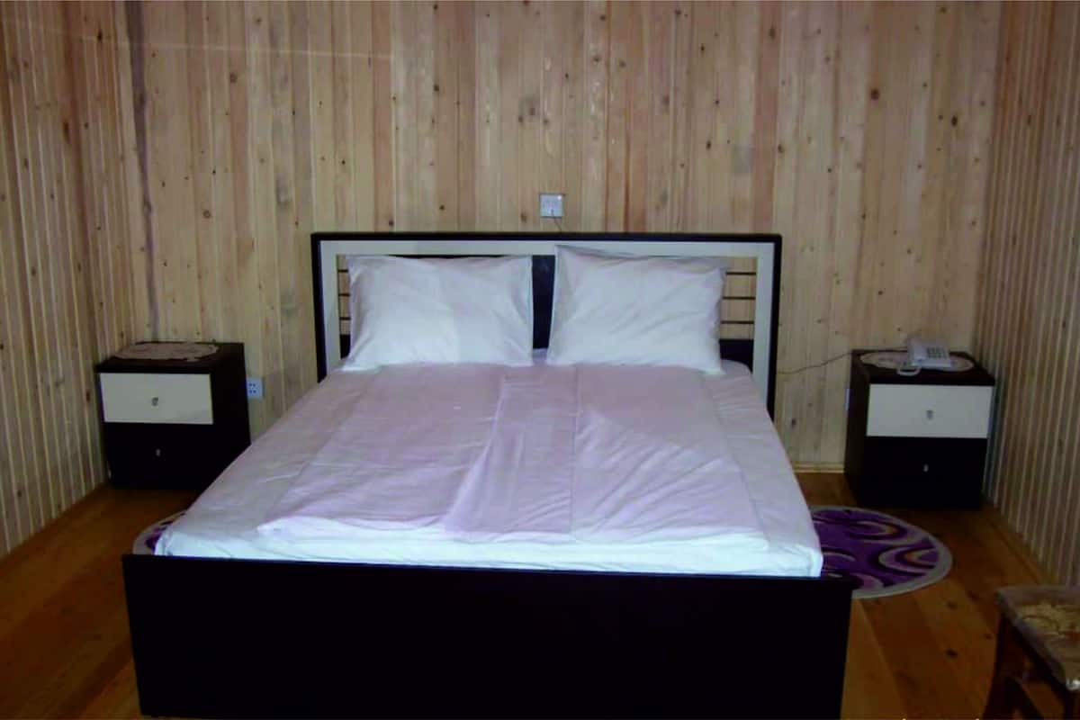 Ein Schlafzimmer mit einer holzverkleideten Wand, einem Bett mit weißer Bettwäsche, zwei Nachttischen und einem violetten Teppich.