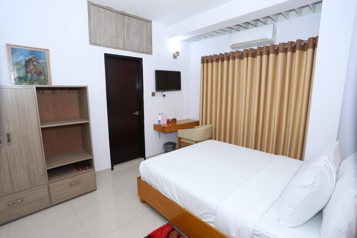 A bedroom with a bed, a wardrobe, a desk, a chair, a television, and a curtain.