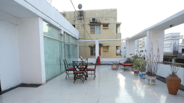 A rooftop terrace with a table and chairs, potted plants, and a view of surrounding buildings. - Hotel Blue Castle (Dhaka)