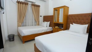 A hotel room with two single beds, a wooden wardrobe, a small trash bin, and an air conditioning unit. - Hotel Blue Castle (Dhaka)