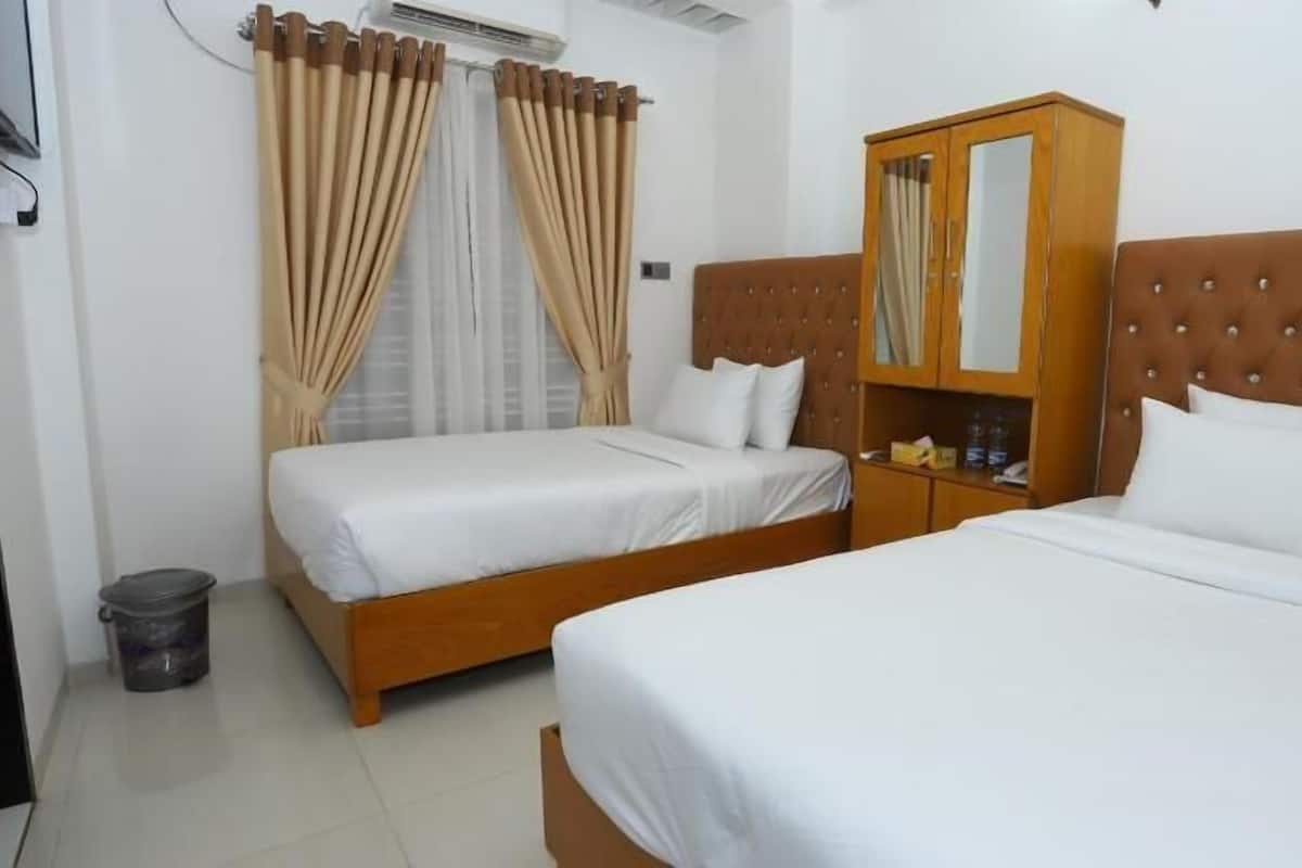 A hotel room with two single beds, a wooden wardrobe, a small trash bin, and an air conditioning unit.