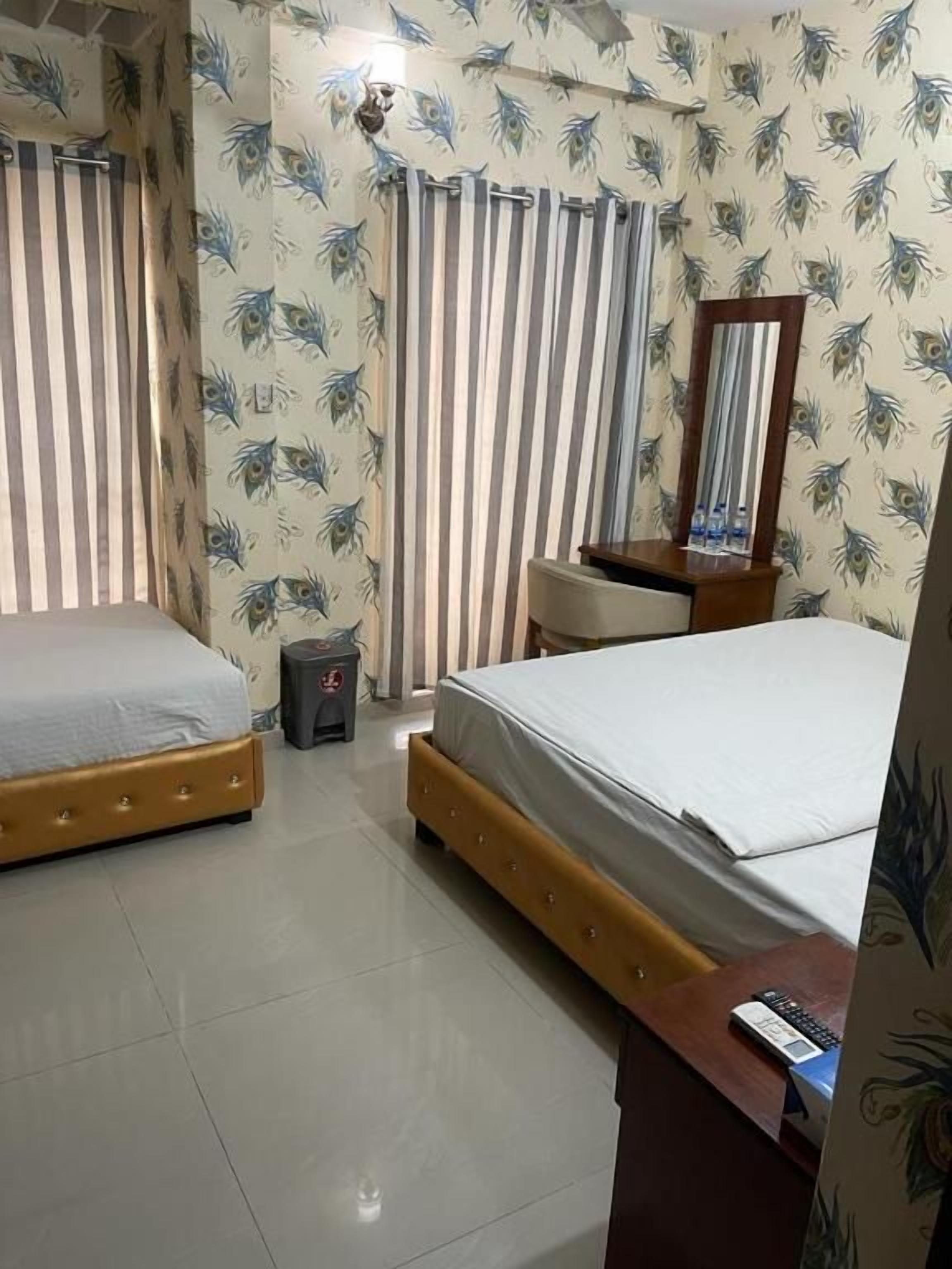 A bedroom with two beds, a mirror, a bedside table, and curtains.