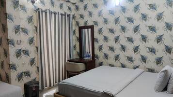 A hotel room with a bed, a desk, a chair, a mirror, and a curtain.