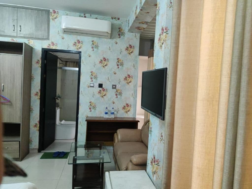 Una sala de estar con un sofá, una mesa de centro de vidrio, un televisor de pantalla plana montado en la pared y un mueble de madera.