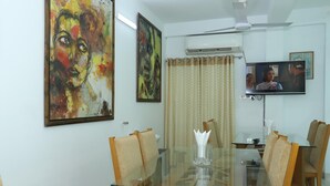 A dining area with a glass table, wooden chairs, and a television mounted on the wall. - Hotel Blue Castle (Dhaka)
