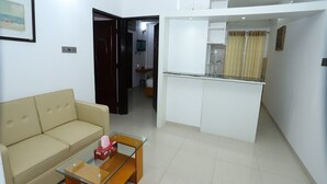A living room with a sofa and a glass-top coffee table, a kitchenette with a countertop and cabinets, and a door leading to another room. - Hotel Blue Castle (Dhaka)