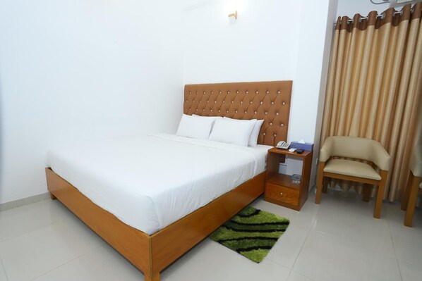 A neatly made bed with a wooden headboard, a bedside table with a lamp, a chair, and a green rug.