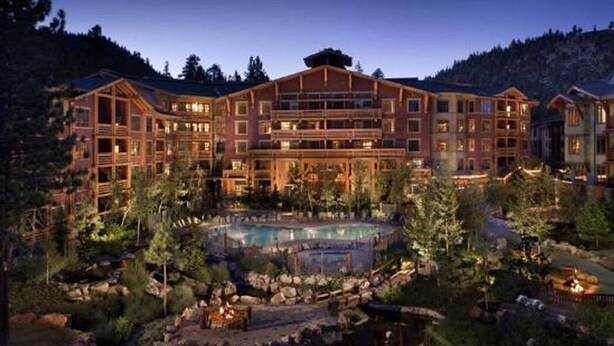 Un grand chalet à étages, une cour intérieure avec une piscine et un paysage montagneux en toile de fond.