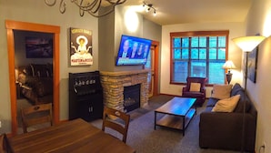 Un salon chaleureux avec une cheminée en pierre, un téléviseur fixé au mur et un coin salon confortable avec un canapé et des fauteuils.
