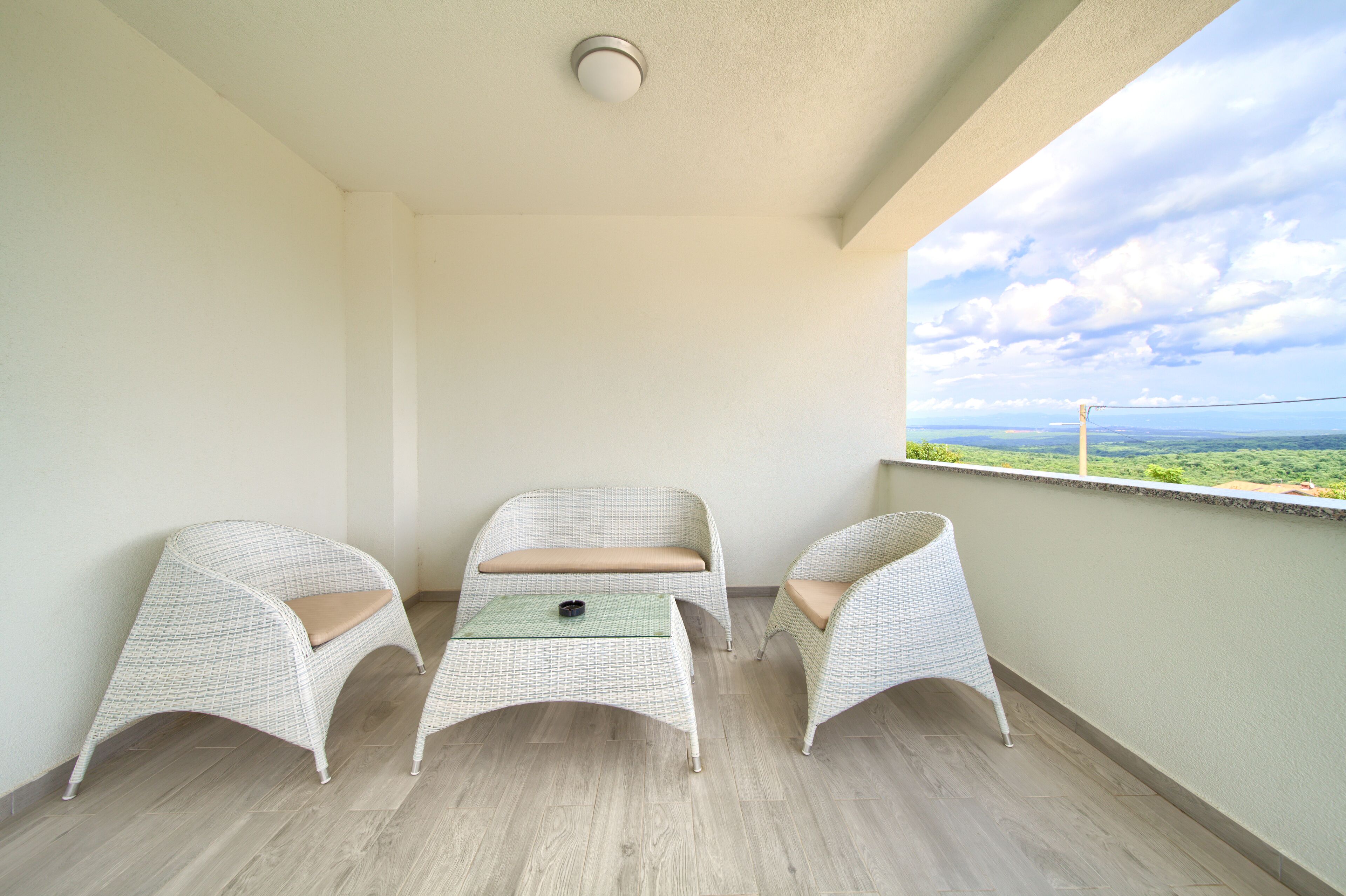 A balcony with two wicker chairs and a small table, overlooking a scenic landscape.