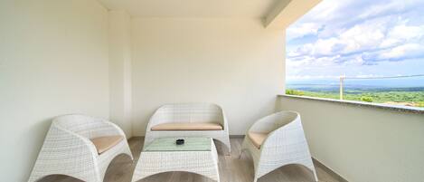 A balcony with two wicker chairs and a small table, overlooking a scenic landscape.