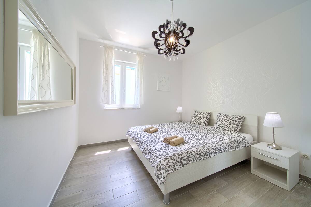 A bedroom with a bed, bedside tables, a chandelier, and a window with curtains.