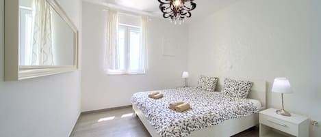 Un dormitorio con cama, mesitas de noche, candelabro y ventana con cortinas.