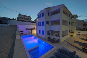 A modern two-story building with a swimming pool, outdoor seating, and a well-maintained garden. - Apartments Mali Nono (Krk)