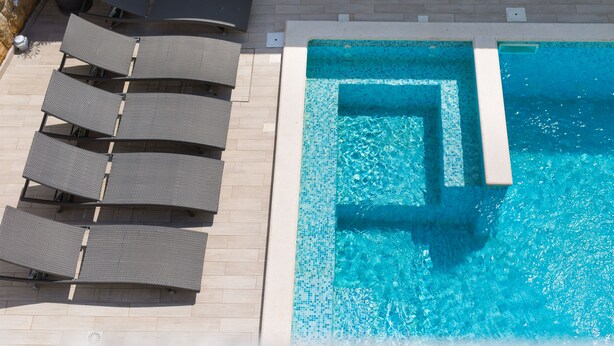 A swimming pool with a tiled edge, surrounded by lounge chairs and a tiled deck. - Apartments Mali Nono (Krk)
