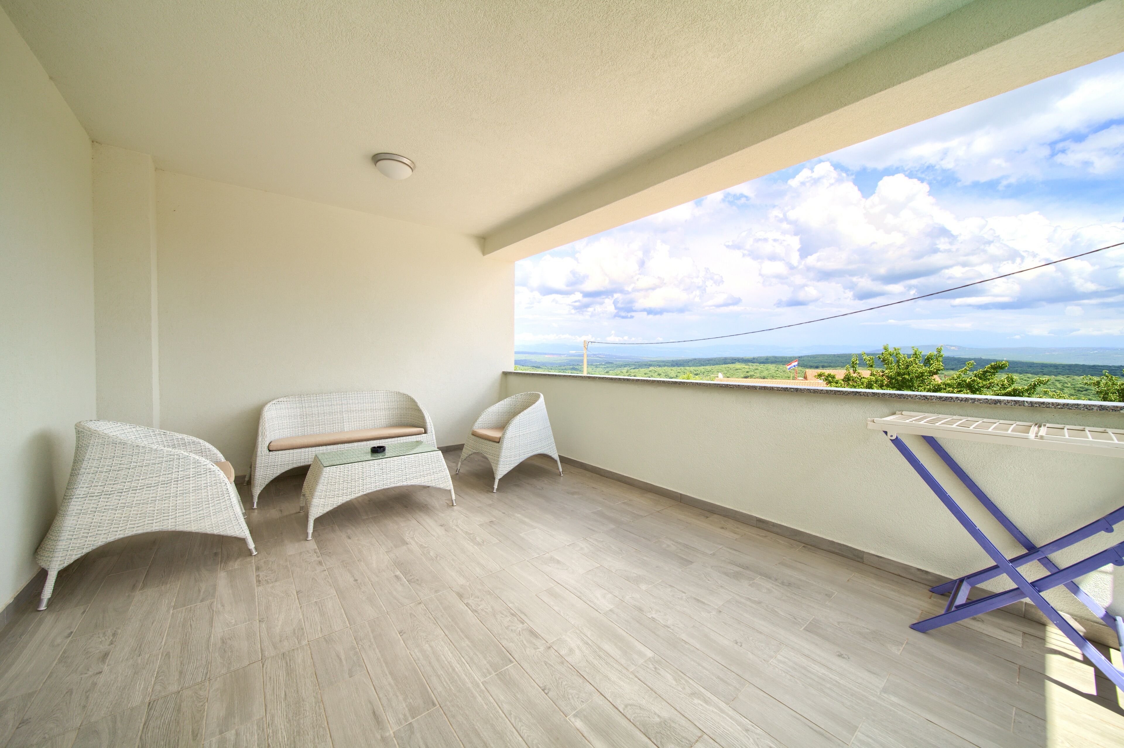 Un balcon avec trois chaises en osier, une petite table et un étendoir.