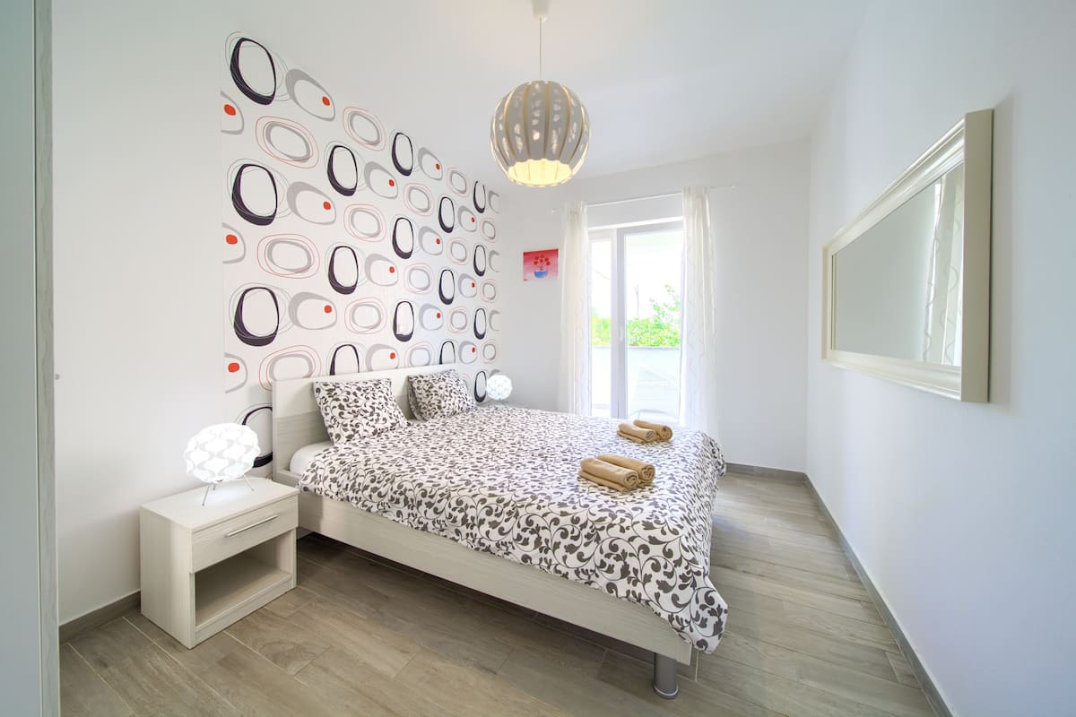 A bedroom with a patterned bedspread, a bedside table with a lamp, and a wall with circular designs.