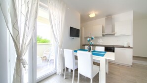A modern kitchen with white cabinets, a flat-screen TV, and a dining area with a table and chairs. - Apartments Mali Nono (Krk)