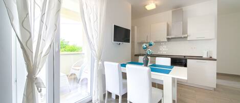 Una cocina moderna con armarios blancos, un televisor de pantalla plana y un comedor con mesa y sillas.