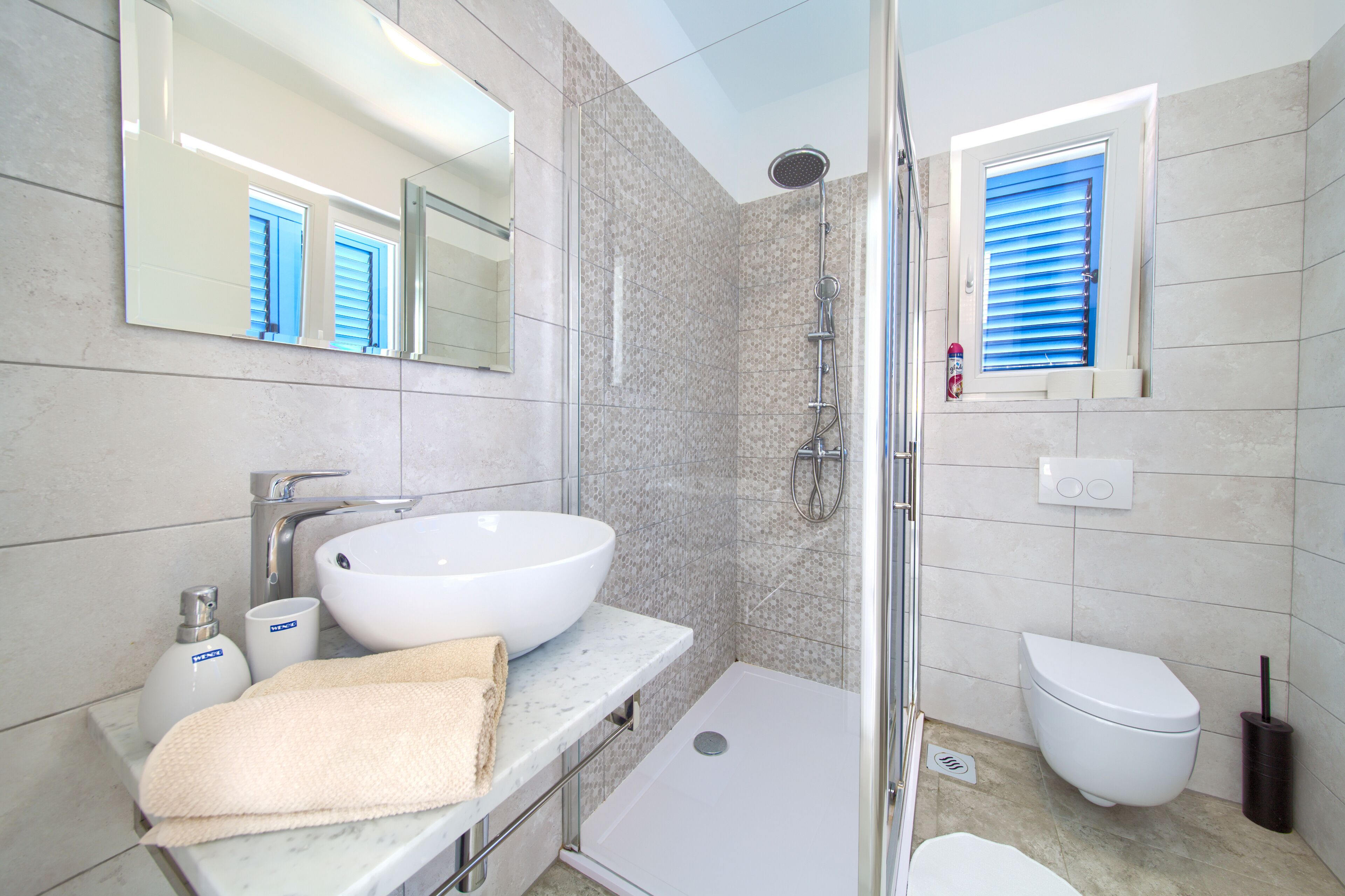 Une salle de bain avec un lavabo blanc, un grand miroir, une douche et des toilettes.
