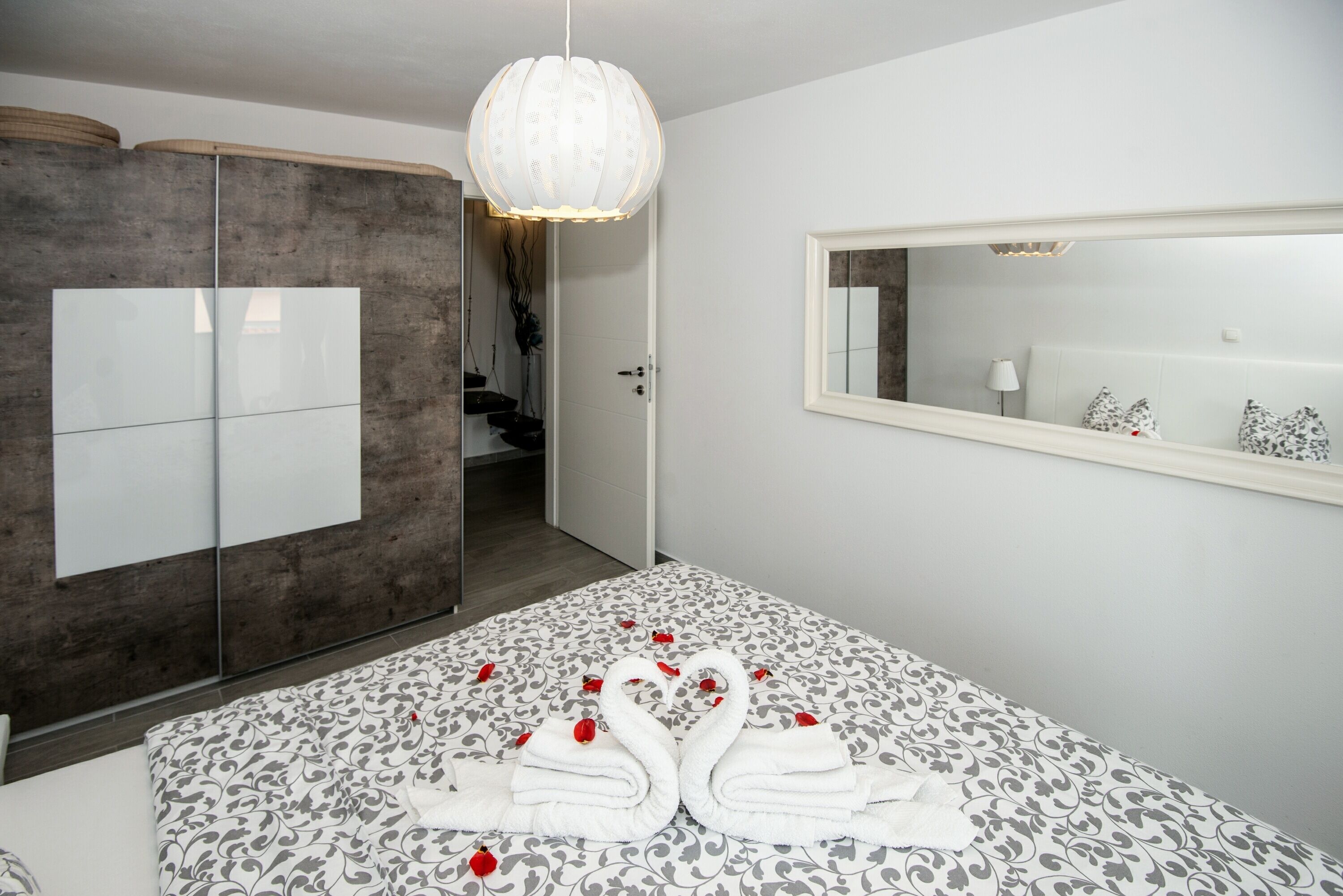 Une chambre d’hôtel moderne avec un grand lit, une armoire, un miroir et un lustre.
