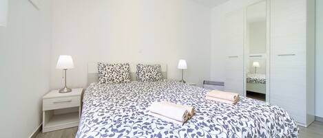 A neatly arranged bedroom with a large bed, two bedside tables with lamps, a mirror, and a wardrobe.