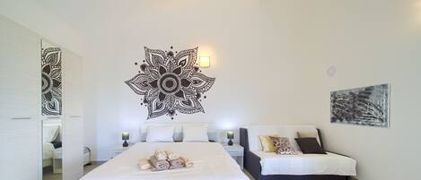 A modern bedroom with a large bed, a sofa, a wall art piece, and a mirror.