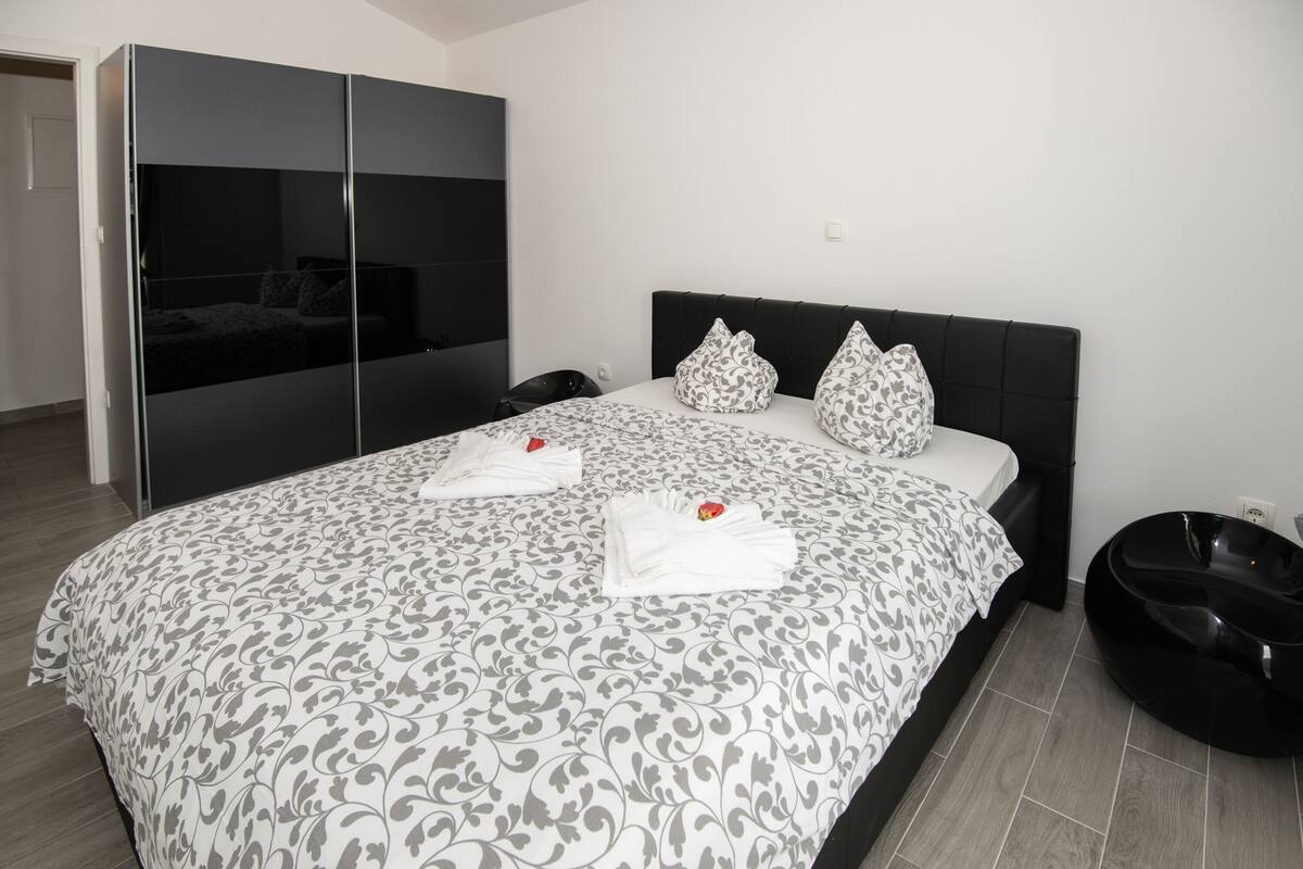 A modern bedroom with a large bed, a wardrobe, and a black bathtub.