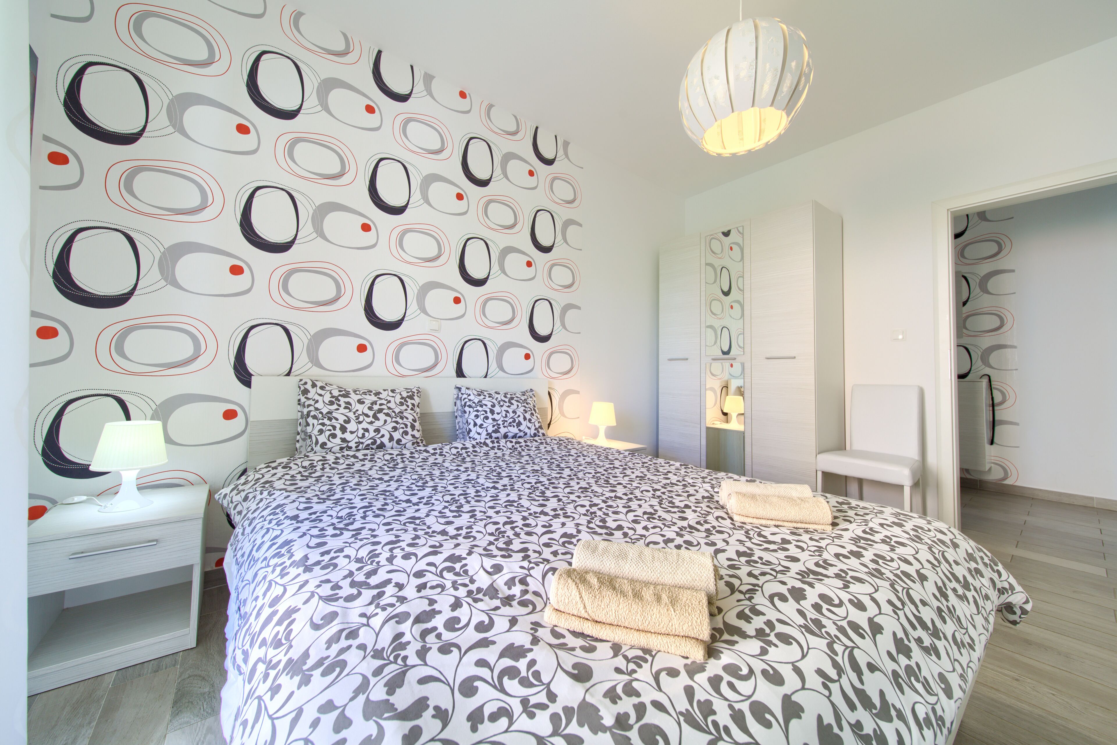 A modern bedroom with a patterned wall, a large bed, bedside tables, and a hanging light fixture.